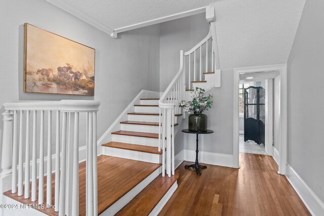 stairway featuring a textured ceiling, ornamental molding, and wood-type flooring