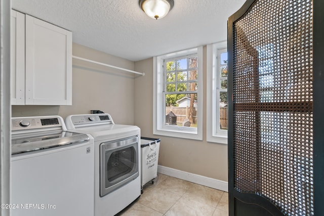 laundry area with washing machine and clothes dryer, a textured ceiling, cabinets, and light tile patterned floors