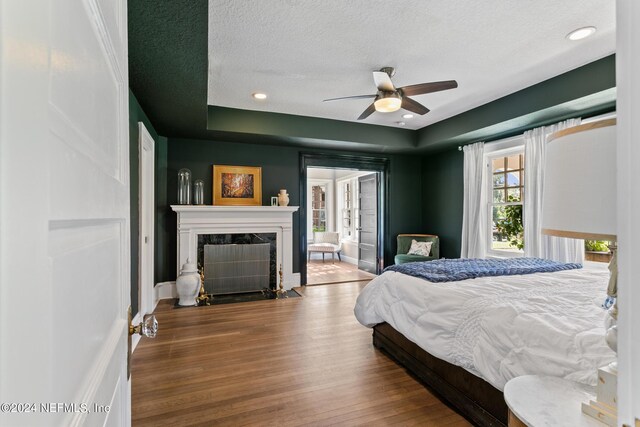 bedroom featuring a textured ceiling, a premium fireplace, hardwood / wood-style floors, and ceiling fan