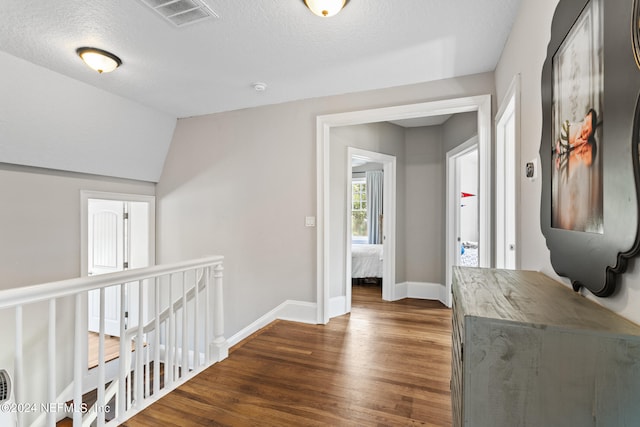 hallway featuring vaulted ceiling, dark hardwood / wood-style flooring, and a textured ceiling