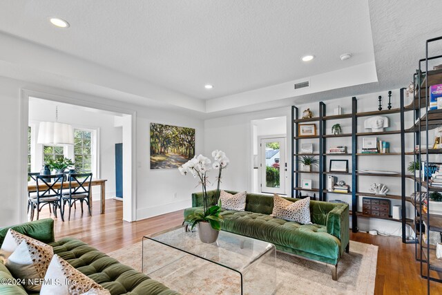 living room featuring a raised ceiling, hardwood / wood-style floors, and a healthy amount of sunlight