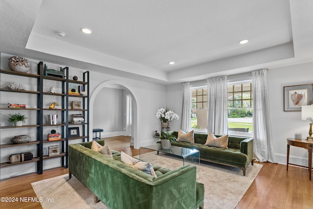 living room with light hardwood / wood-style flooring, a tray ceiling, and a textured ceiling