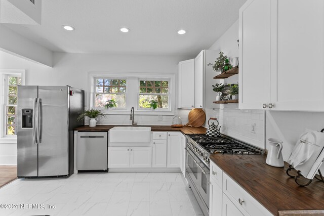 kitchen with decorative backsplash, range with two ovens, dishwashing machine, stainless steel fridge, and wooden counters