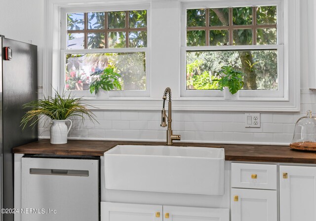 kitchen featuring dishwasher, sink, butcher block counters, and stainless steel refrigerator