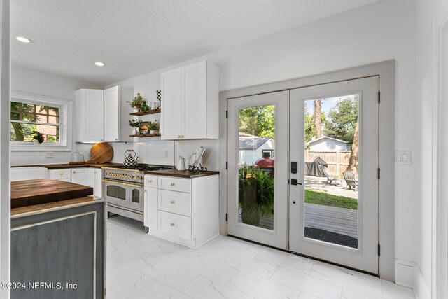 kitchen featuring decorative backsplash, white cabinetry, french doors, light tile patterned flooring, and double oven range