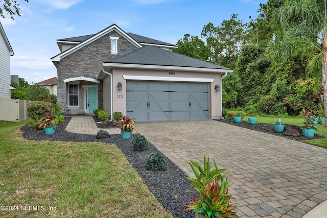 view of front of house featuring an attached garage, stucco siding, a front lawn, stone siding, and decorative driveway