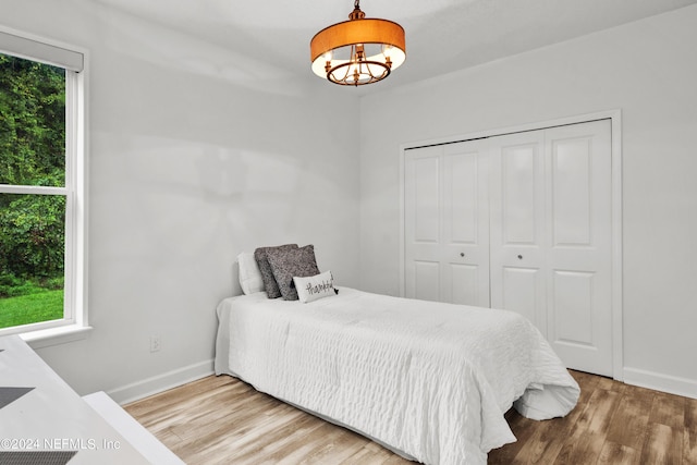 bedroom with a closet, baseboards, an inviting chandelier, and wood finished floors