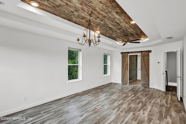 empty room featuring visible vents, a raised ceiling, wood finished floors, a barn door, and baseboards