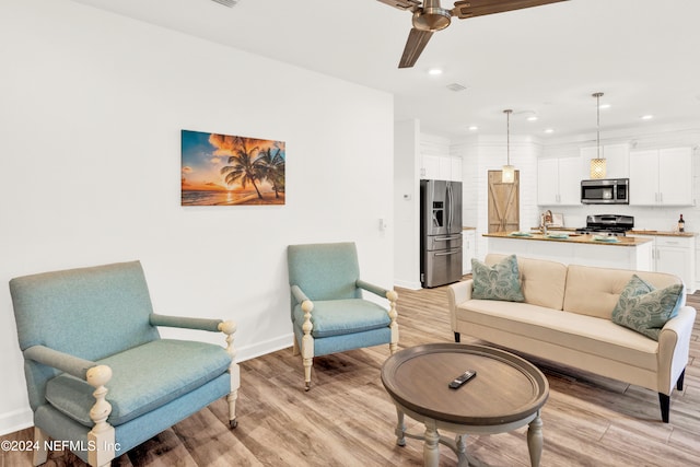 living room featuring ceiling fan, light hardwood / wood-style floors, and sink