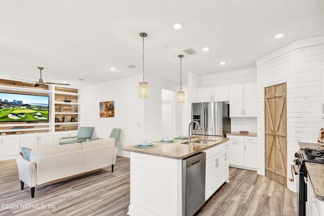 kitchen featuring hanging light fixtures, stainless steel appliances, a center island with sink, white cabinets, and sink