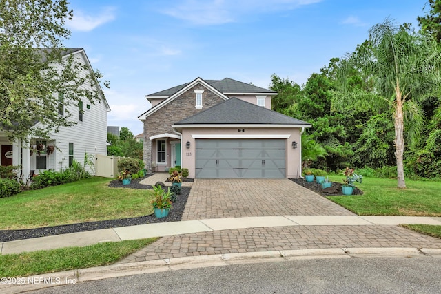 traditional-style home featuring a front yard, decorative driveway, stone siding, and an attached garage