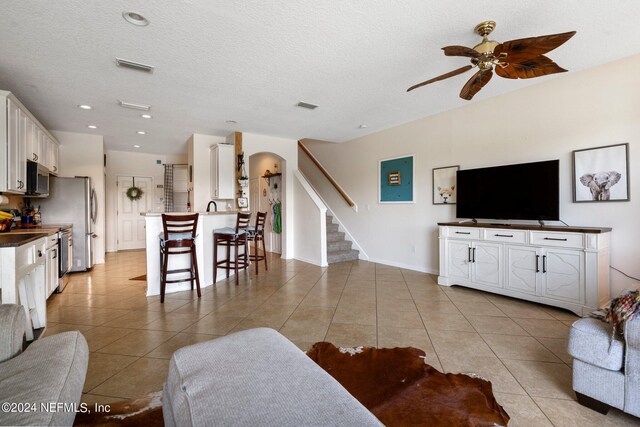 living room with a textured ceiling, ceiling fan, and light tile patterned floors