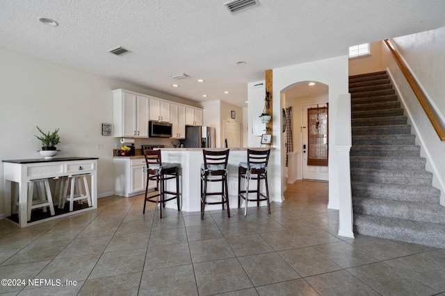 kitchen featuring appliances with stainless steel finishes, dark tile patterned floors, white cabinets, and a kitchen bar