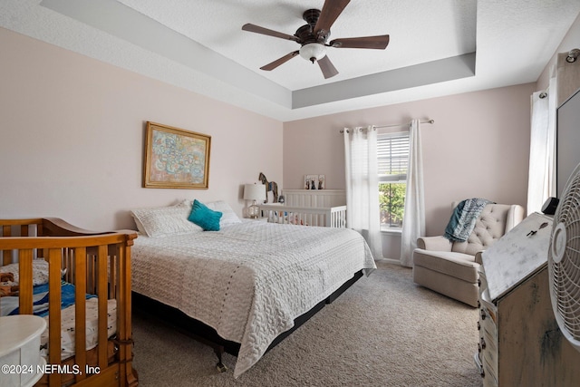 carpeted bedroom featuring ceiling fan and a raised ceiling