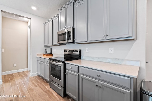 kitchen featuring gray cabinets, light hardwood / wood-style floors, light stone countertops, a textured ceiling, and stainless steel appliances