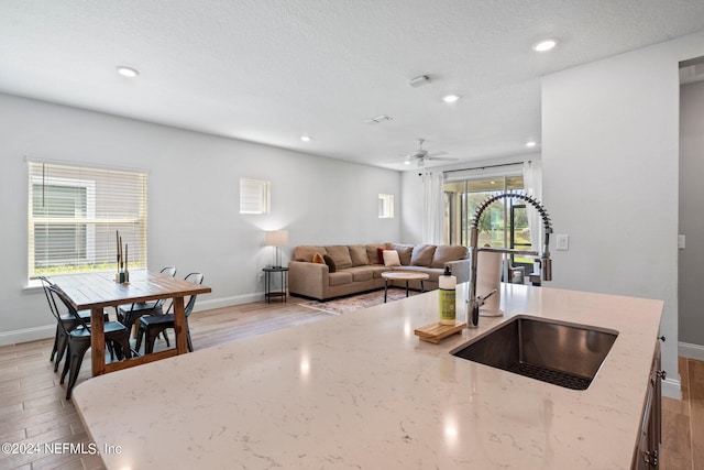 kitchen featuring sink, light wood-type flooring, light stone countertops, and ceiling fan