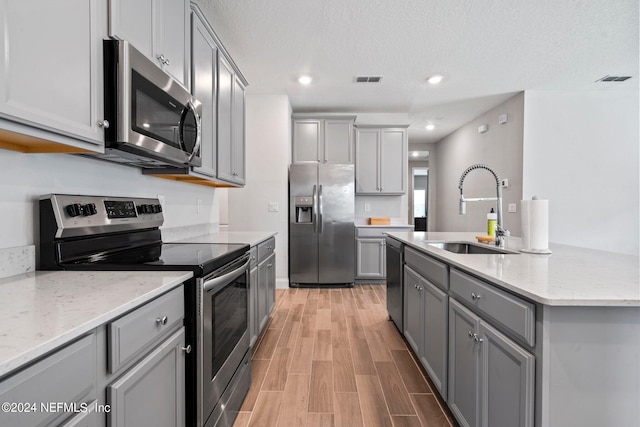 kitchen with sink, appliances with stainless steel finishes, light stone countertops, light hardwood / wood-style floors, and gray cabinets