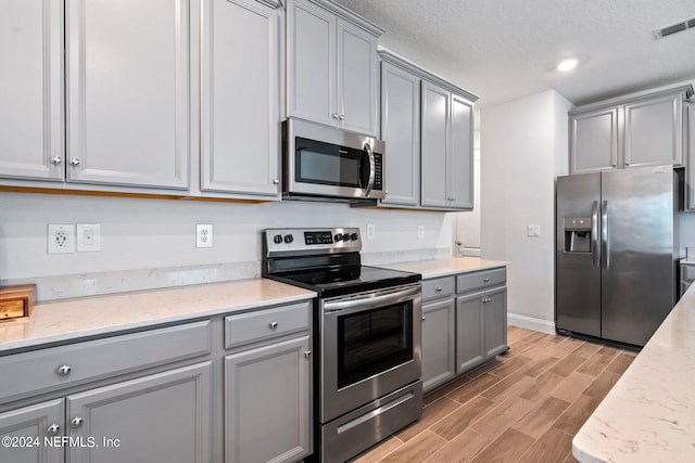 kitchen with gray cabinets, stainless steel appliances, light hardwood / wood-style flooring, and light stone counters