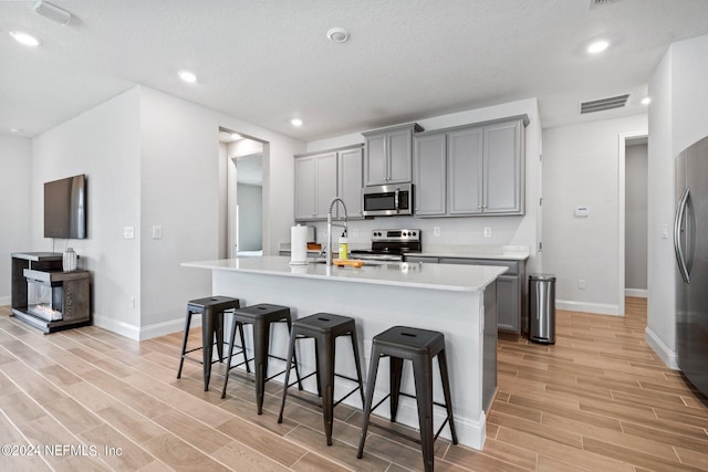 kitchen featuring stainless steel appliances, a kitchen bar, light wood-type flooring, a kitchen island with sink, and gray cabinets