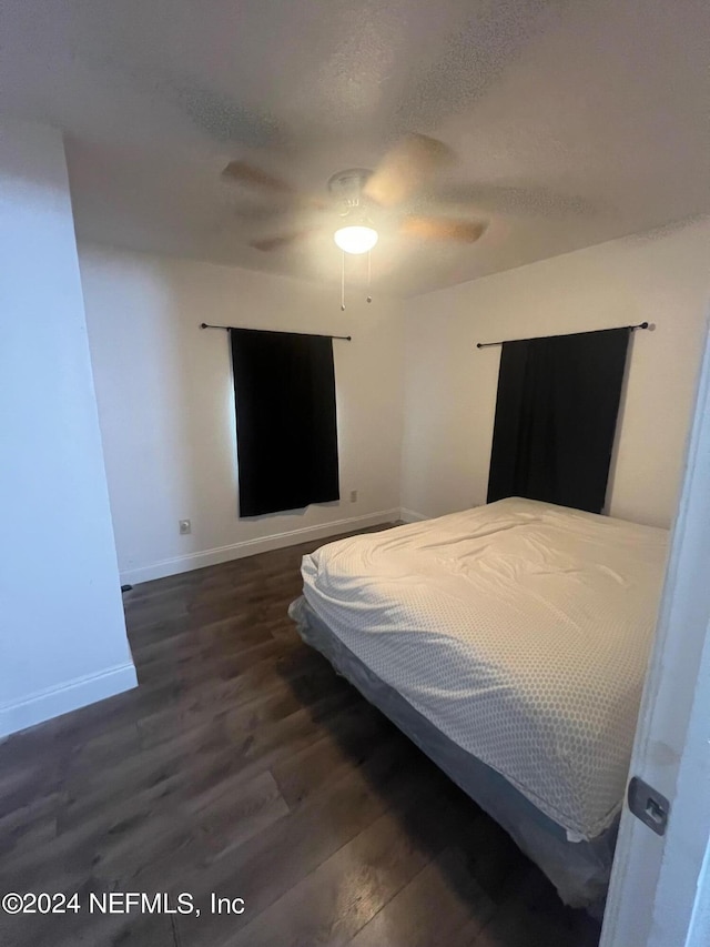 bedroom with a textured ceiling, ceiling fan, and dark hardwood / wood-style floors