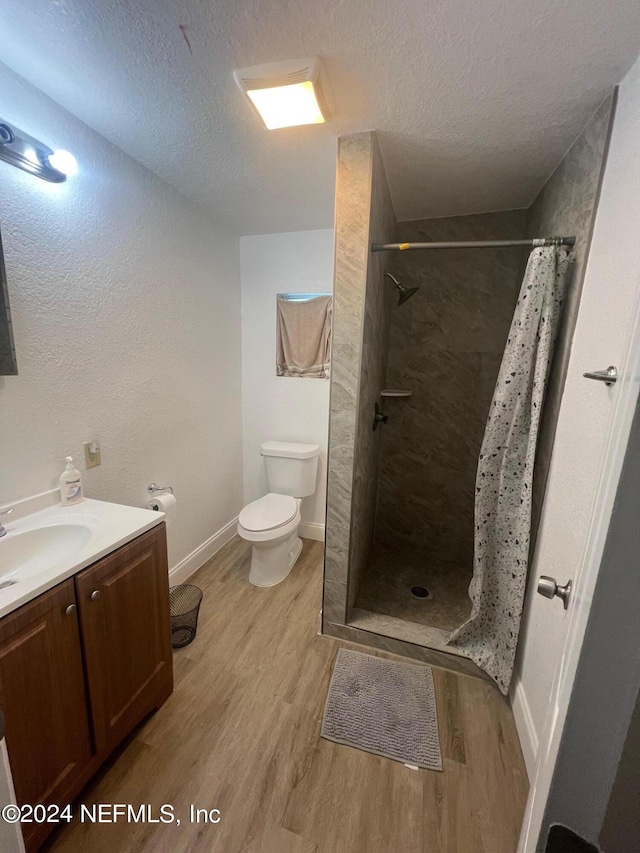 bathroom featuring a textured ceiling, vanity, hardwood / wood-style floors, toilet, and a shower with curtain