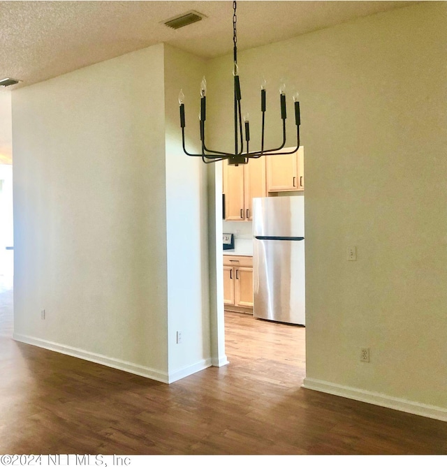 unfurnished dining area featuring a textured ceiling, an inviting chandelier, and light hardwood / wood-style floors