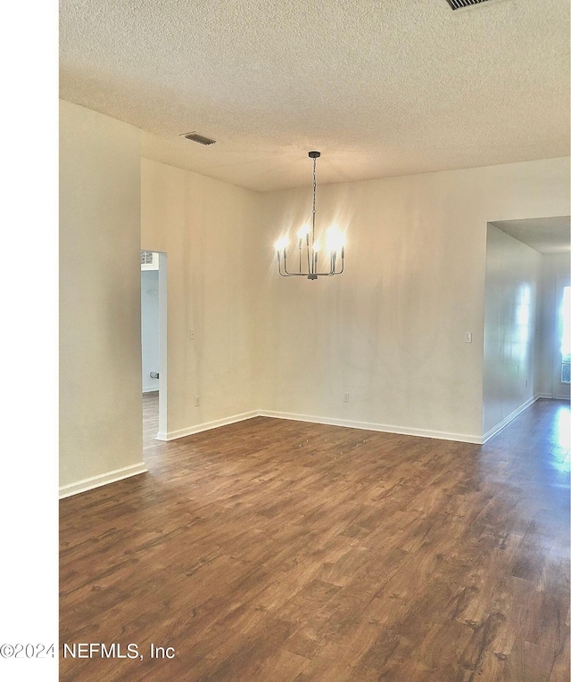 unfurnished room featuring dark wood-type flooring, a textured ceiling, and a chandelier