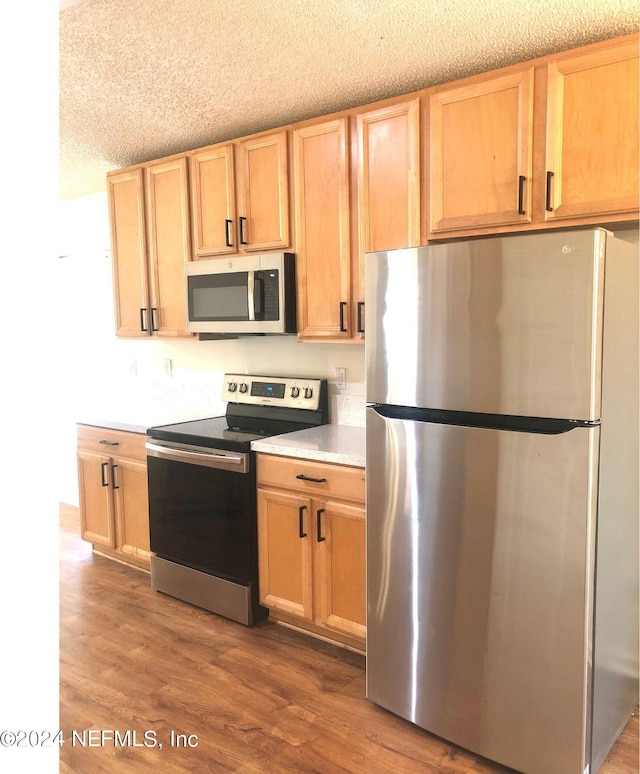 kitchen with appliances with stainless steel finishes, dark hardwood / wood-style flooring, light brown cabinets, and a textured ceiling