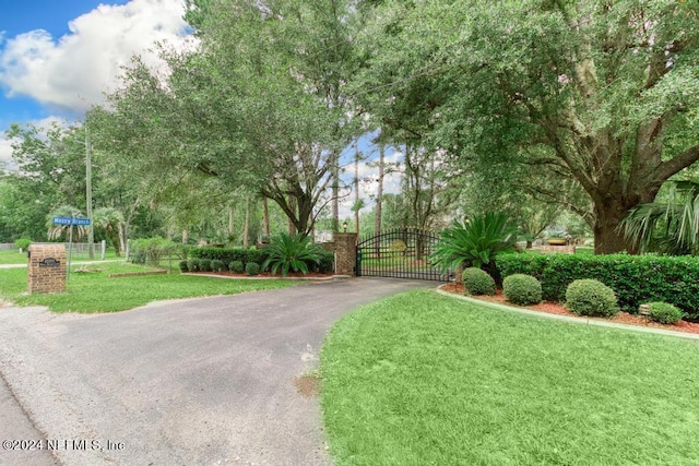 view of property's community featuring a gate, aphalt driveway, fence, and a lawn