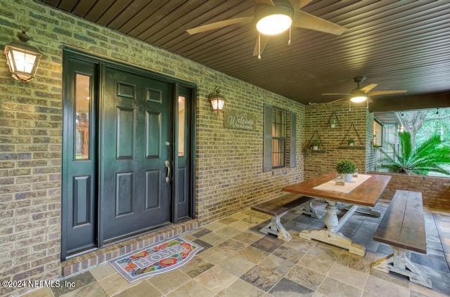 view of exterior entry featuring a ceiling fan, brick siding, and outdoor dining space