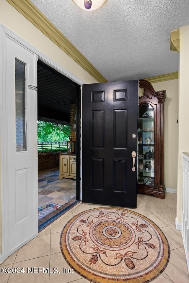 entryway featuring light tile patterned flooring, a textured ceiling, ornamental molding, and baseboards