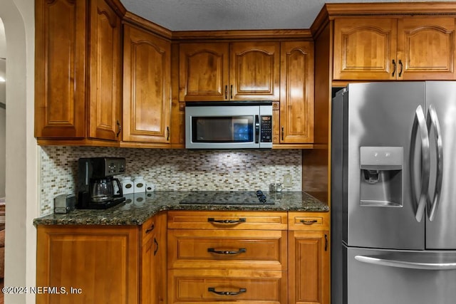 kitchen with appliances with stainless steel finishes, dark stone counters, and tasteful backsplash