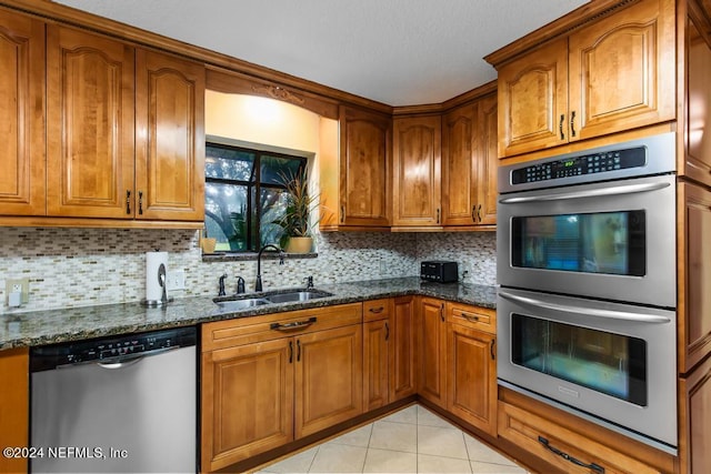 kitchen with brown cabinetry, dark stone countertops, a sink, and stainless steel appliances