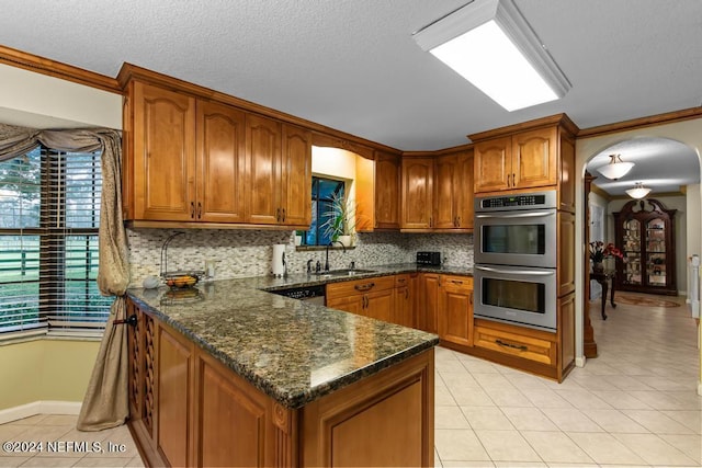 kitchen with a sink, double oven, a peninsula, brown cabinets, and arched walkways