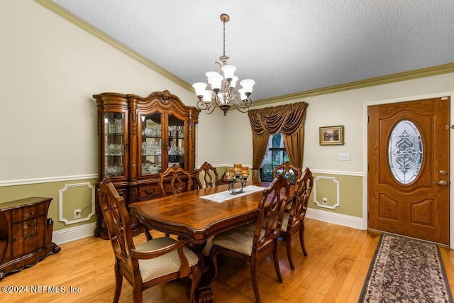 dining room featuring a textured ceiling, ornamental molding, light wood-type flooring, and a chandelier