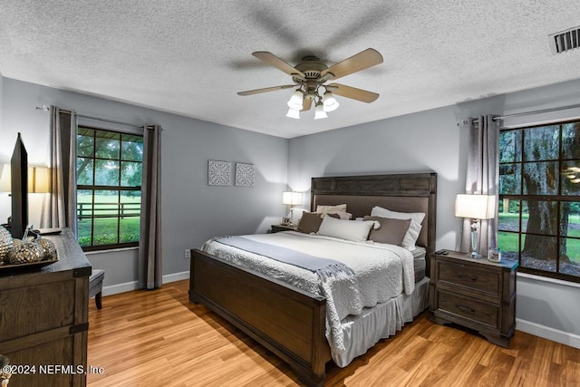 bedroom with baseboards, a textured ceiling, ceiling fan, light wood-style flooring, and visible vents