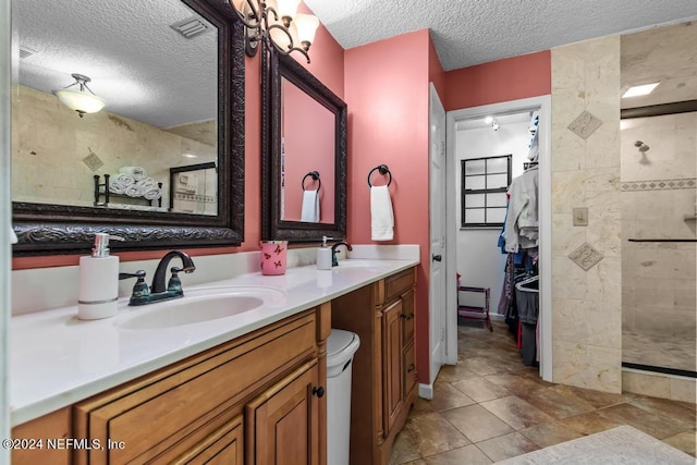 bathroom with double vanity, tiled shower, a sink, and a textured ceiling
