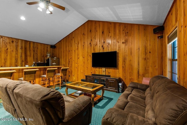 living room featuring vaulted ceiling, wood walls, carpet floors, and ceiling fan