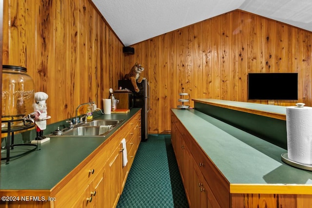 kitchen with a textured ceiling, vaulted ceiling, sink, dark colored carpet, and wooden walls