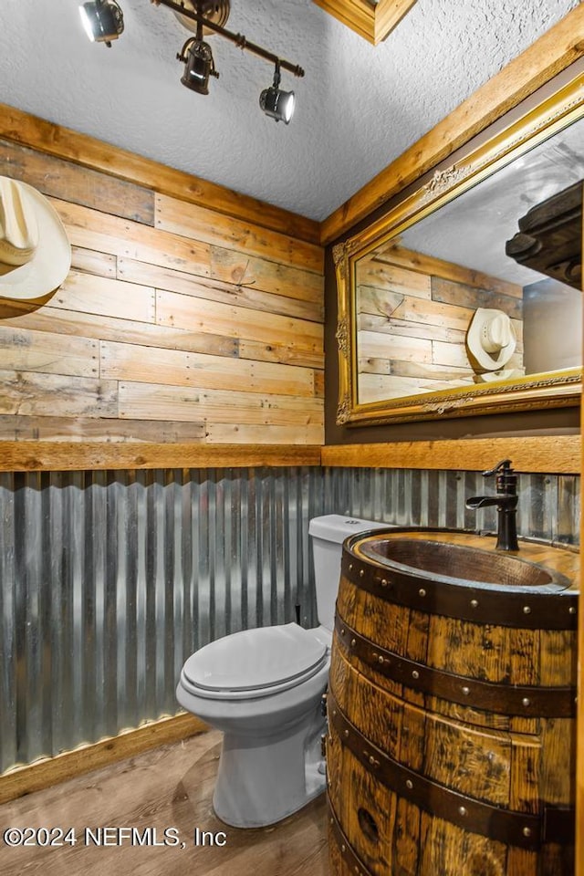 bathroom featuring a textured ceiling, wood walls, toilet, wood finished floors, and vanity