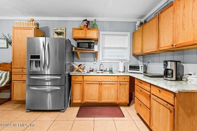 kitchen with light tile patterned floors, appliances with stainless steel finishes, light stone countertops, sink, and a textured ceiling