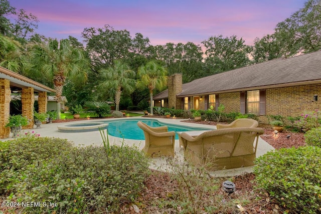 pool at dusk with a pool with connected hot tub and a patio area