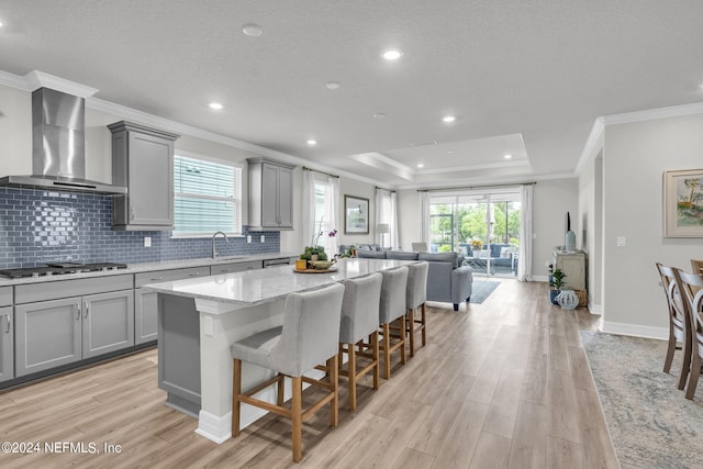 kitchen with wall chimney exhaust hood, a breakfast bar, a center island, gray cabinets, and stainless steel gas stovetop