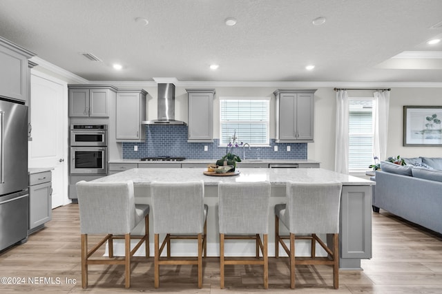 kitchen with stainless steel appliances, gray cabinets, a center island, and wall chimney range hood