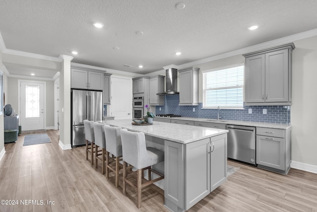 kitchen featuring appliances with stainless steel finishes, a center island, wall chimney range hood, and gray cabinetry