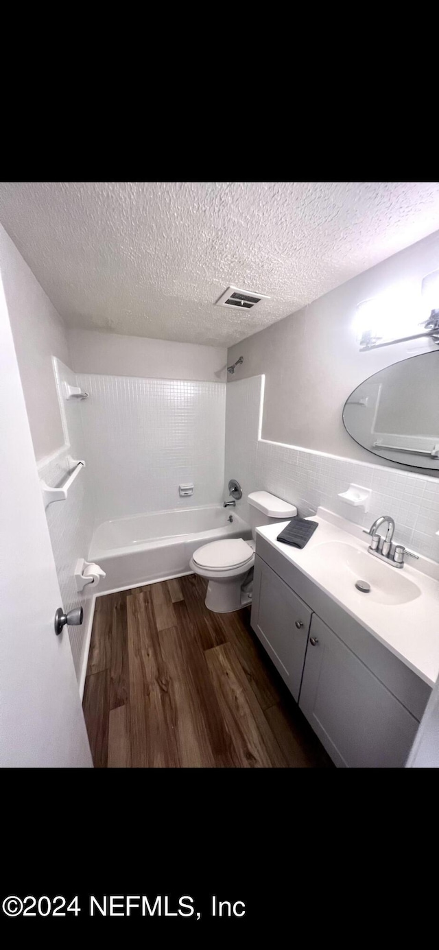bathroom with a textured ceiling, shower / bathtub combination, toilet, wood finished floors, and vanity