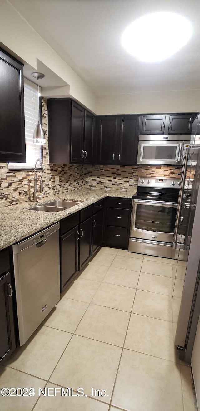 kitchen with stainless steel appliances, light stone counters, backsplash, and a sink