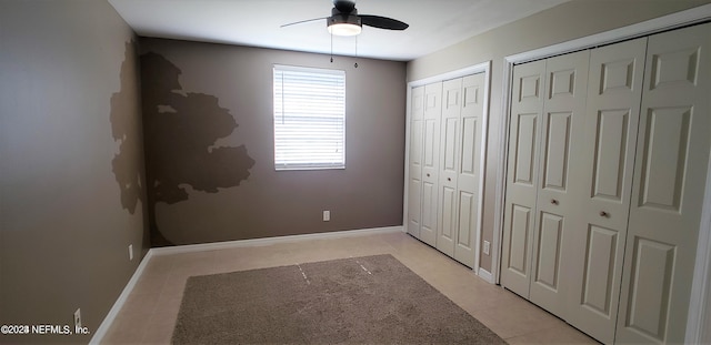 unfurnished bedroom with multiple closets, ceiling fan, baseboards, and light tile patterned floors