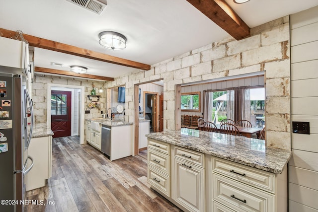 kitchen with beamed ceiling, light stone counters, stainless steel appliances, cream cabinets, and light hardwood / wood-style flooring