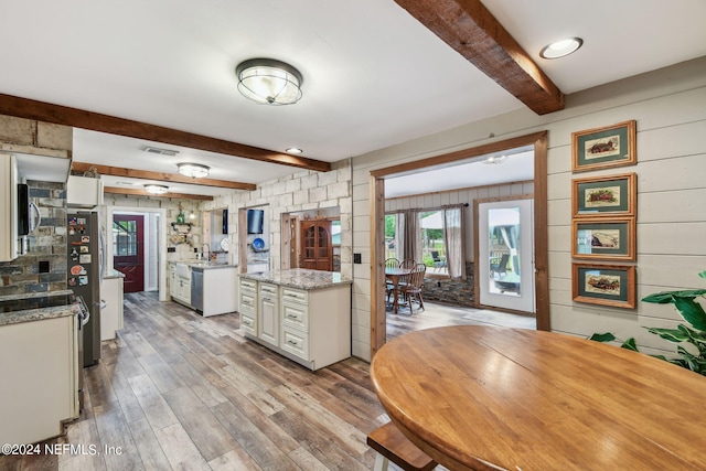 kitchen featuring light wood-type flooring, beamed ceiling, stainless steel appliances, light stone countertops, and white cabinets